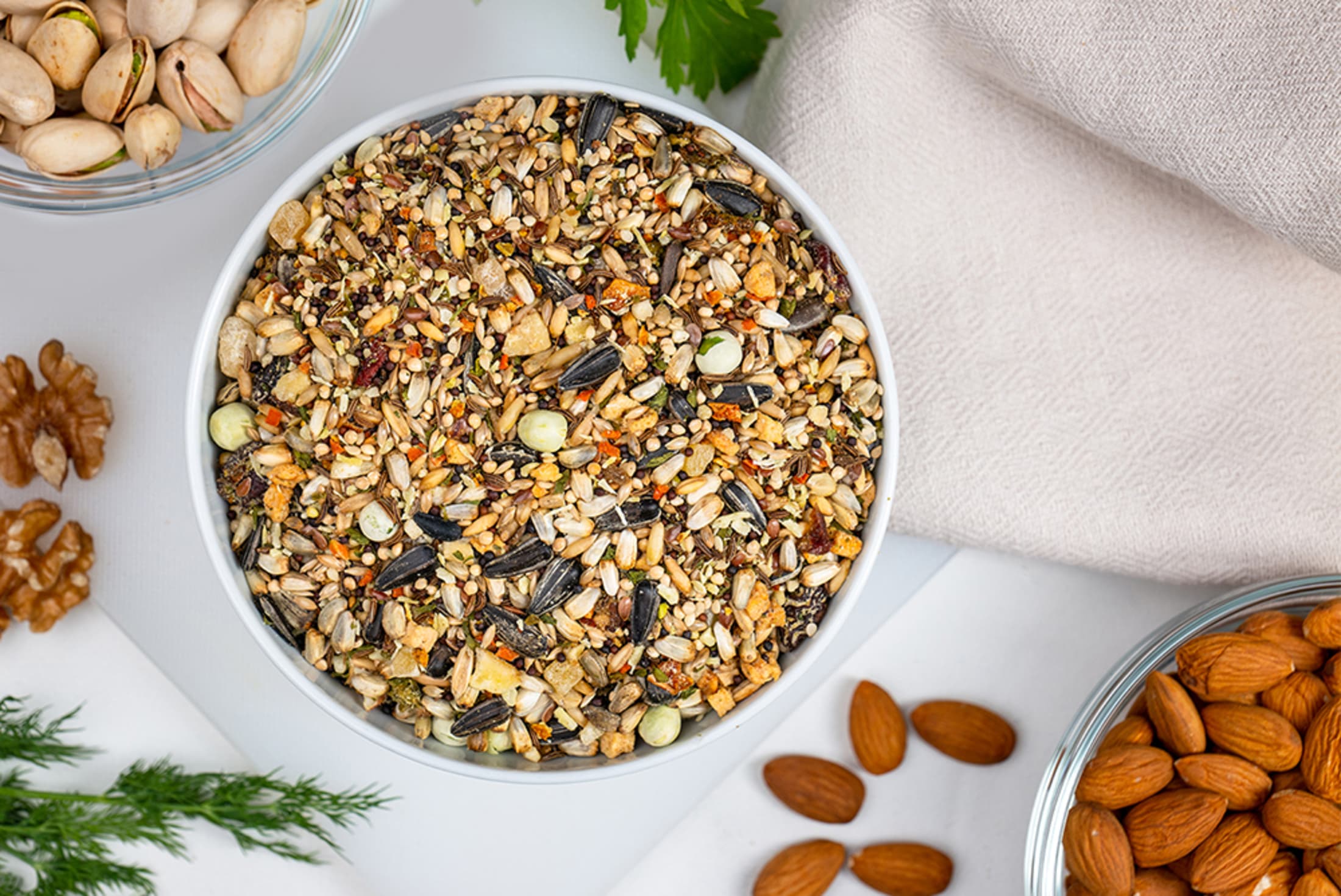 Birdseed mix in a bowl with nuts on a white surface
