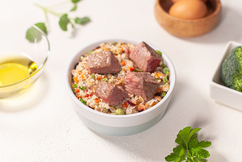 Bowl of beef and vegetable salad on a white table with eggs and oil in the background