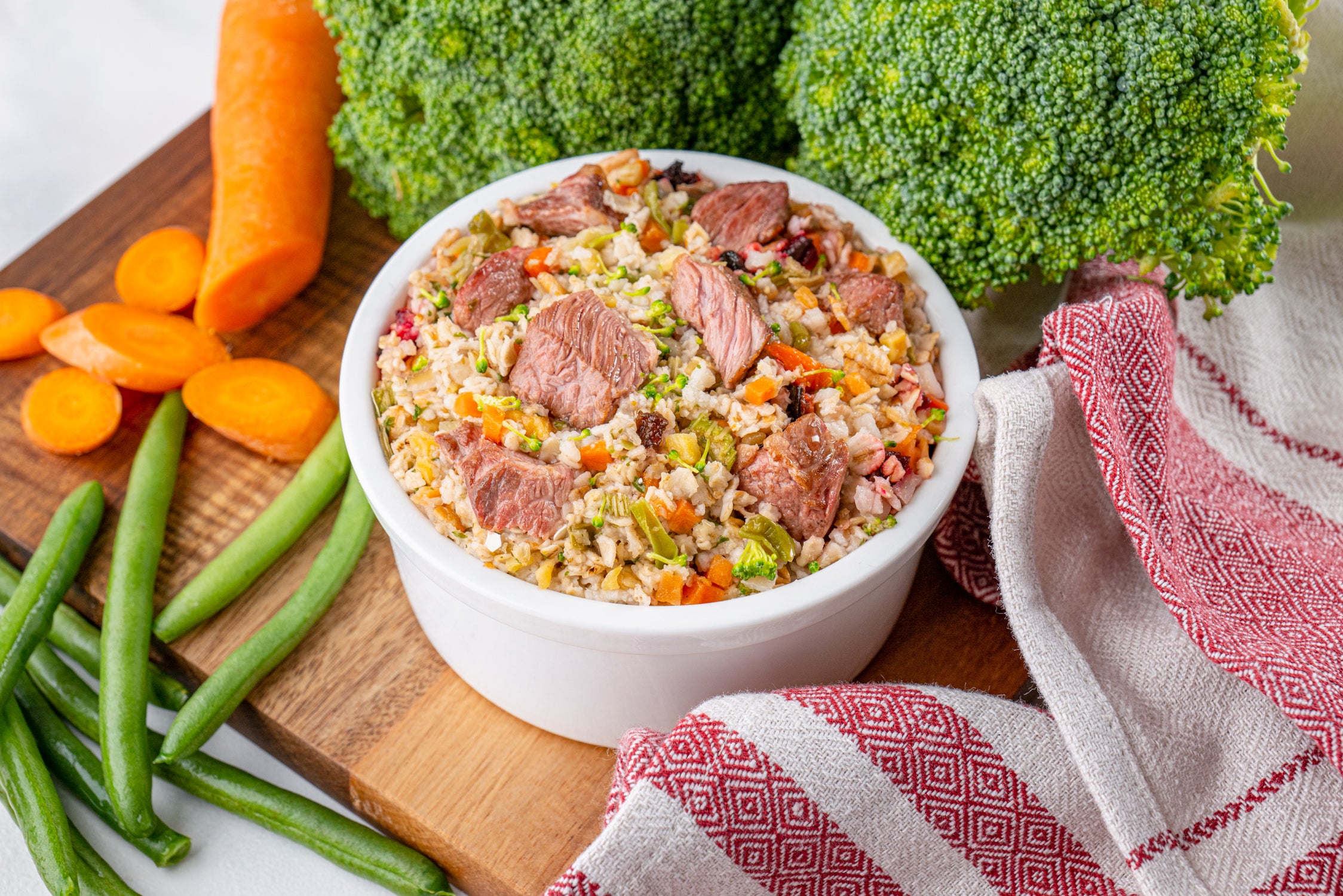 Bowl of beef and vegetable stir-fry on a wooden cutting board with carrots, broccoli, and green beans.