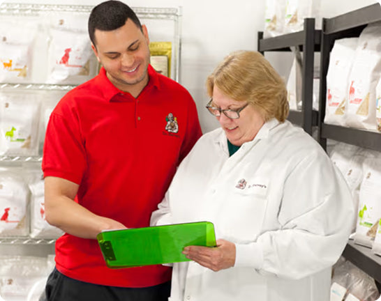 Two people, one in a red shirt and the other in a white coat, looking at a green device in a warehouse setting.