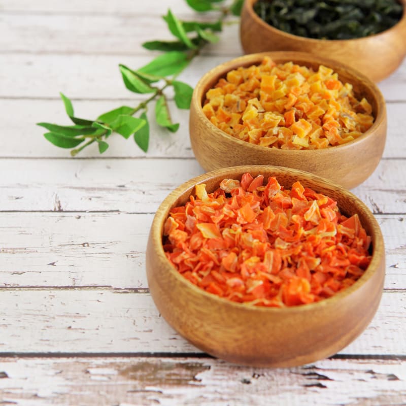 Three wooden bowls filled with different types of dried vegetables on a wooden surface.