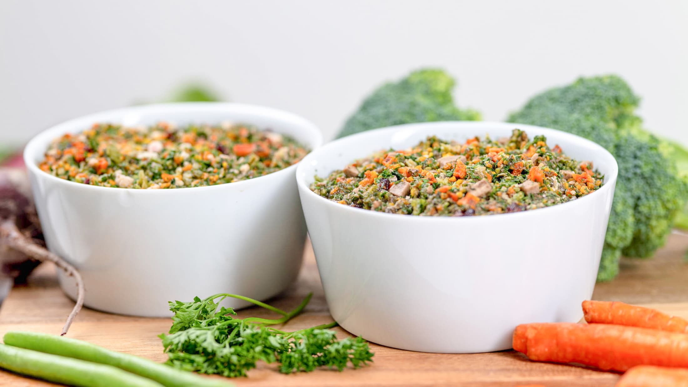 Two white bowls filled with a colorful salad on a wooden surface with vegetables around.