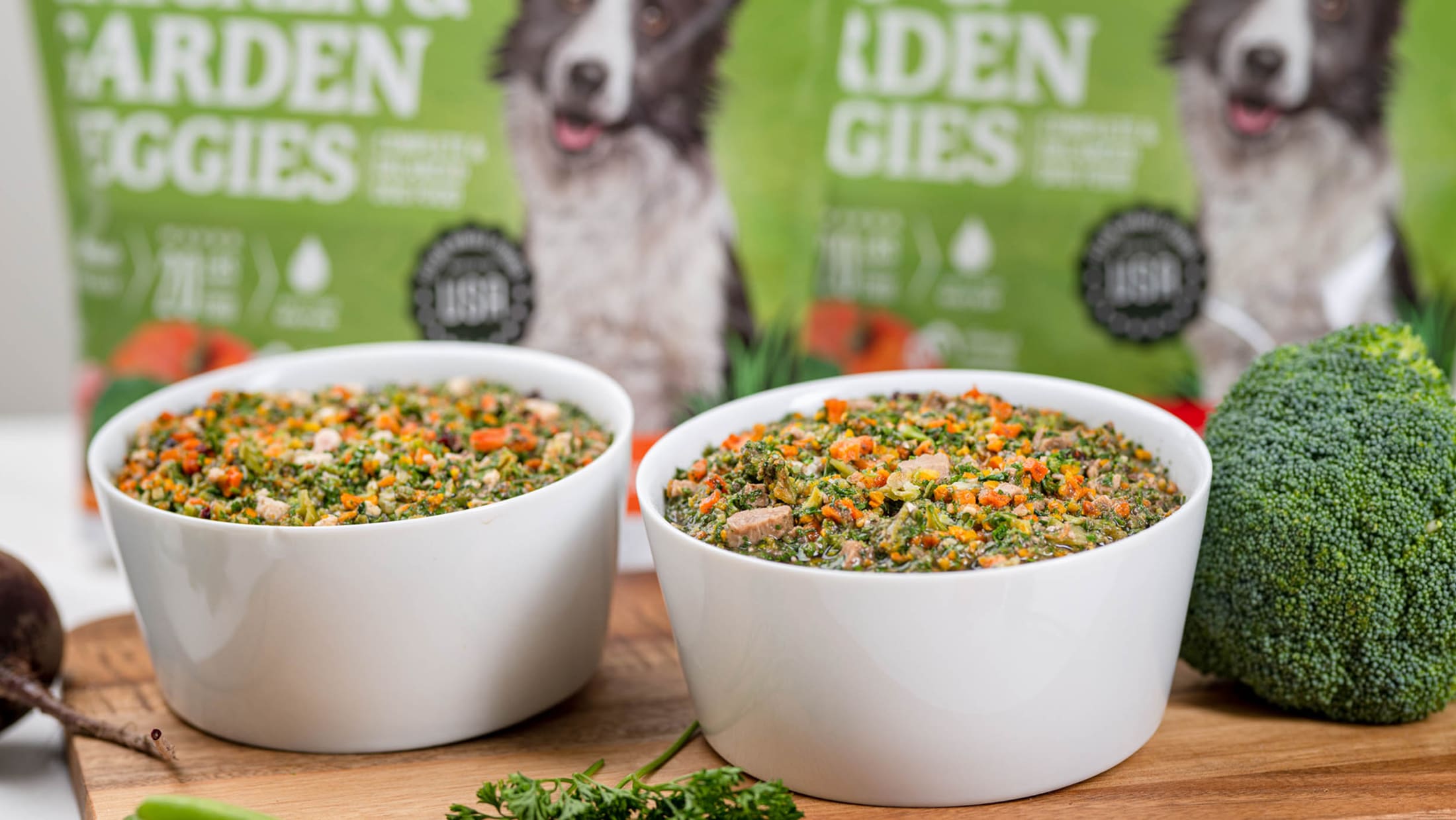 Two bowls of dog food with 'Garden Giggles' packaging in the background.